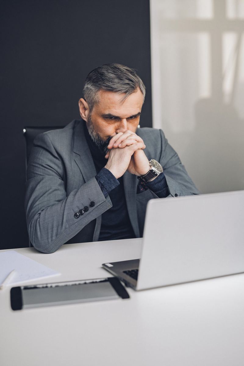 Dono de empresa com as mãos juntas diante do rosto, olhando parado a tela do notebook.