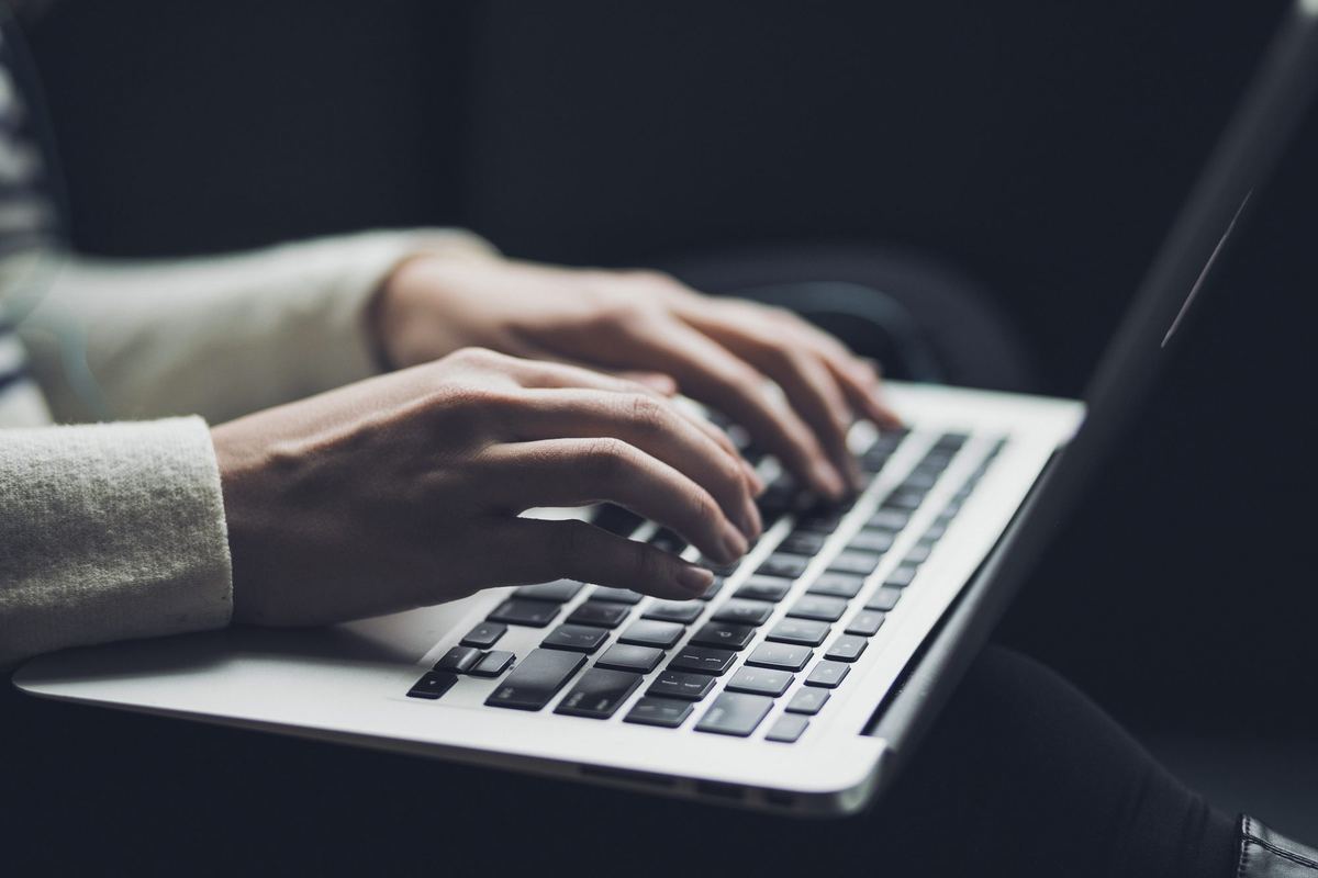 Mãos digitando no teclado de um notebook, em luz baixa.